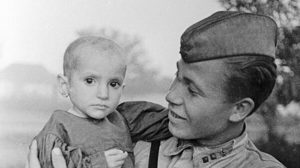 Советский офицер держит на руках спасённую им девочку из деревни Эльхотово Советский офицер держит на руках спасённую им девочку из деревни Эльхотово