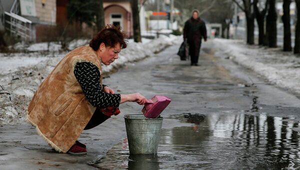 Женщина набирает воду из лужи на улице в Донецке Женщина набирает воду из лужи на улице в Донецке