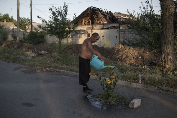 Мужчина поливает цветы на одной из улиц поселка Веселое Донецкой области Мужчина поливает цветы на одной из улиц поселка Веселое Донецкой области