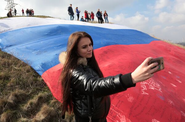 Девушка делает селфи на фоне огромного флага России на фестивале Крымская весна в селе Мирное Симферопольского района Республики Крым Девушка делает селфи на фоне огромного флага России на фестивале Крымская весна в селе Мирное Симферопольского района Республики Крым