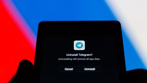 Логотип Telegram на экране смартфона на фоне флага РФ Логотип Telegram на экране смартфона на фоне флага РФ
