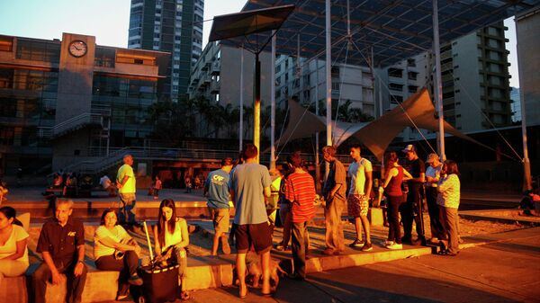 Люди выстроились в очередь к аккумулятору с солнечной панелью на площади в Каракасе, чтобы зарядить телефоны
