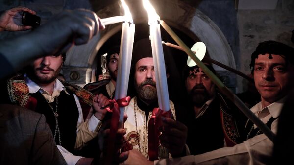 Греческий священнослужитель зажигает свечи верующих Благодатным огнем в церкви в Афинах