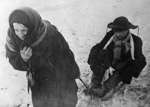 Жители блокадного Ленинграда: женщина везет ослабевшего от голода мужа на санках Жители блокадного Ленинграда: женщина везет ослабевшего от голода мужа на санках
