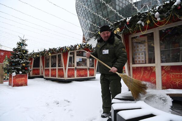 Мужчина убирает снег на площадке фестиваля Путешествие в Рождество в Москве Мужчина убирает снег на площадке фестиваля Путешествие в Рождество в Москве
